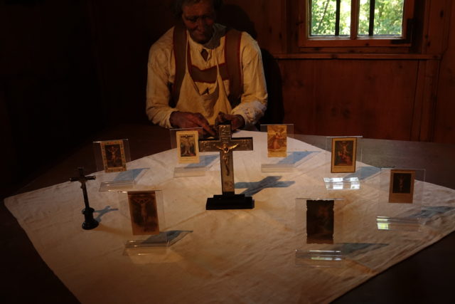 Kruzifixe und Andachtsbildchen mit Kreuzdarstellungen, präsentiert auf dem Tisch in der Stube des Rablhauses