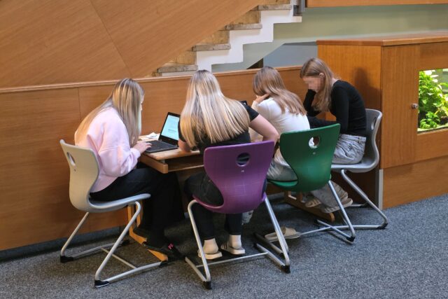 5 Jugendliche an einem tisch, zum Teil mit Laptop, beim Arbeiten