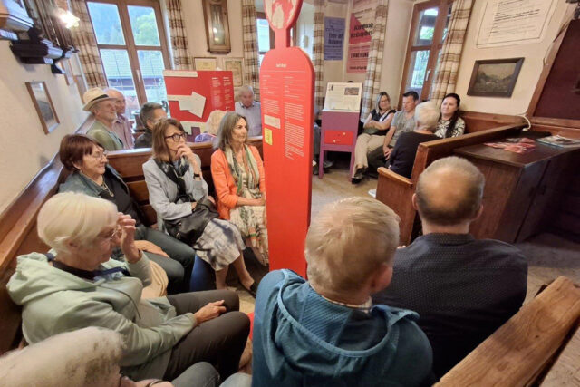 Ausstellungselemente in einer Gaststube, rundum zahlreiche BesucherInnen.