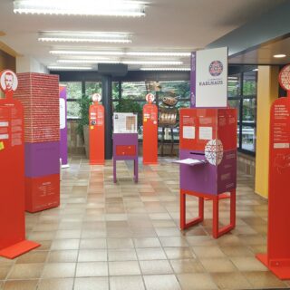 Ausstellungselemente in Violett und Rot in einem großen Raum.