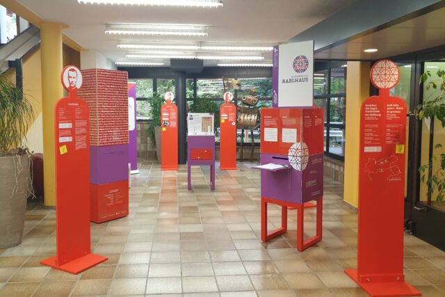 Ausstellungselemente in Violett und Rot in einem großen Raum.